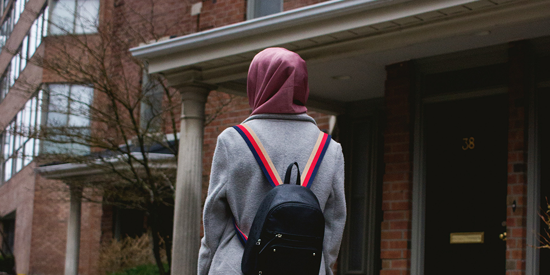 A woman wearing a hijab and backpack looking out at a building