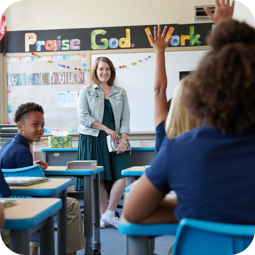 Teacher smiling at students raising hands at desks