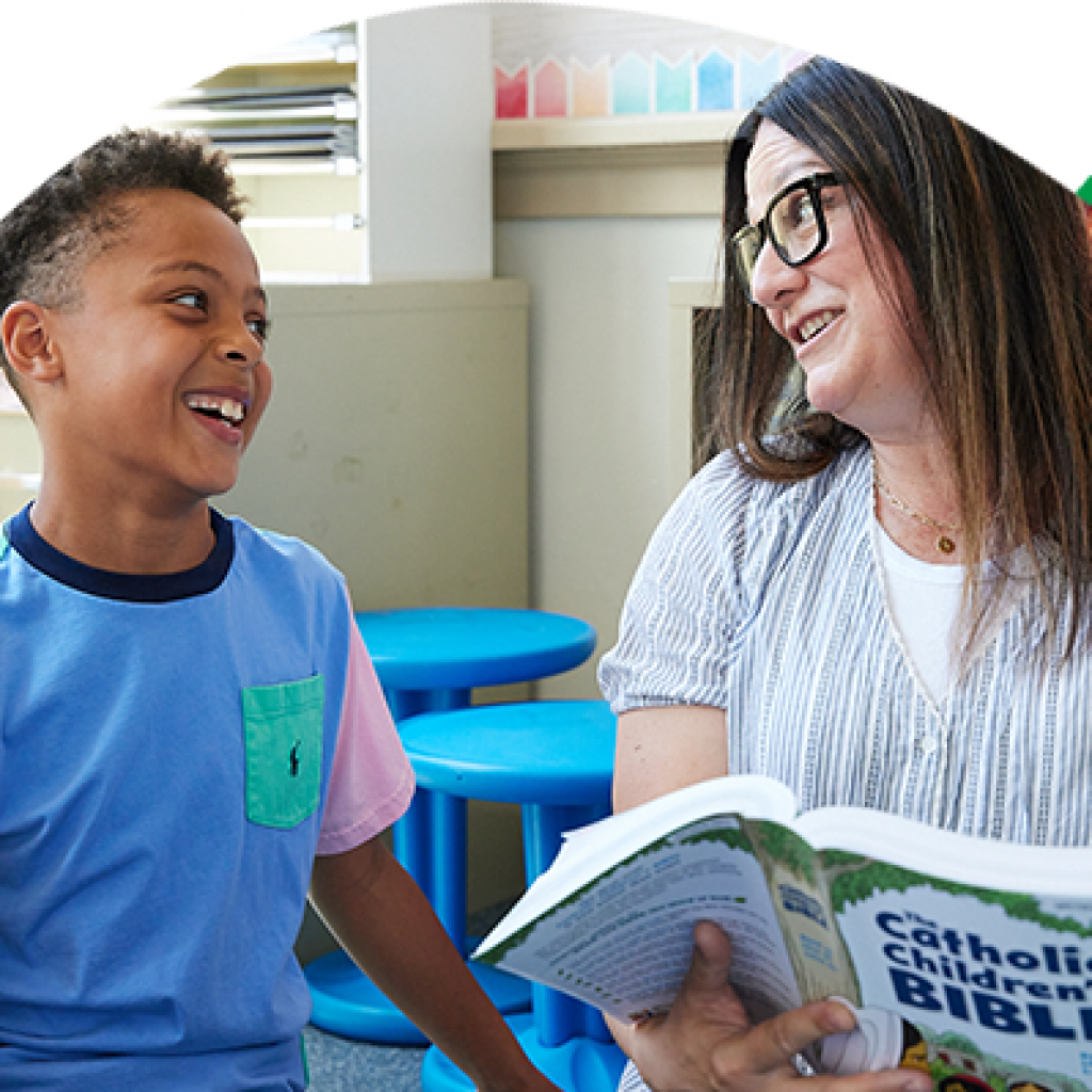 Young person smiling with his mentor reading The Catholic Children’s Bible