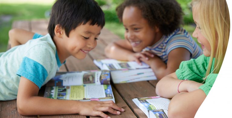 Kids sitting around a picnic table smiling while reading The Catholic Children’s Bible